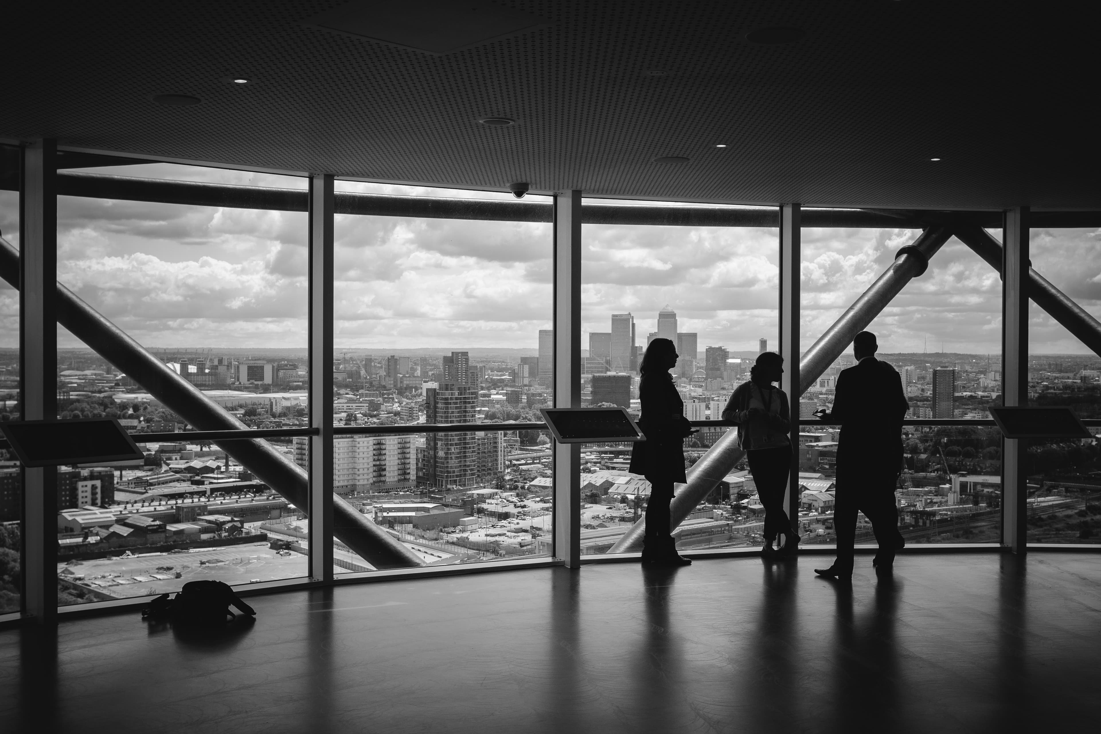 Three colleagues talking beside the floor-to-ceiling window of a high-rise office, city skyline beyond